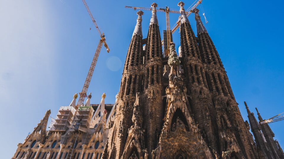 View of Sagrada Familia's intricate facade and cranes against a clear blue sky in Barcelona.