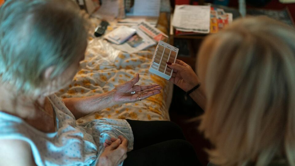 Teknologi til demente An elderly woman receives medication assistance at home, emphasizing home healthcare and caregiver support.