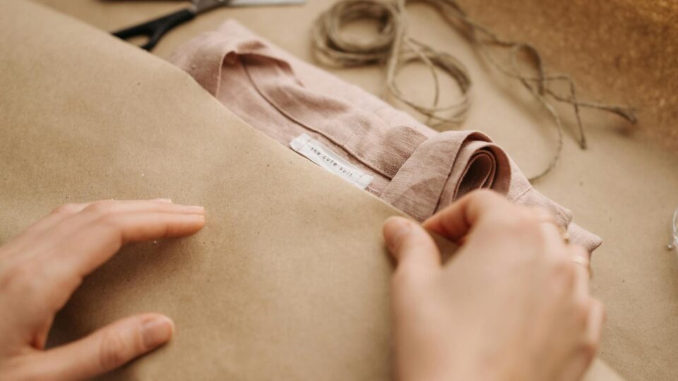 Close-up of hands wrapping a linen shirt with twine, showcasing craftsmanship and sustainable fashion.